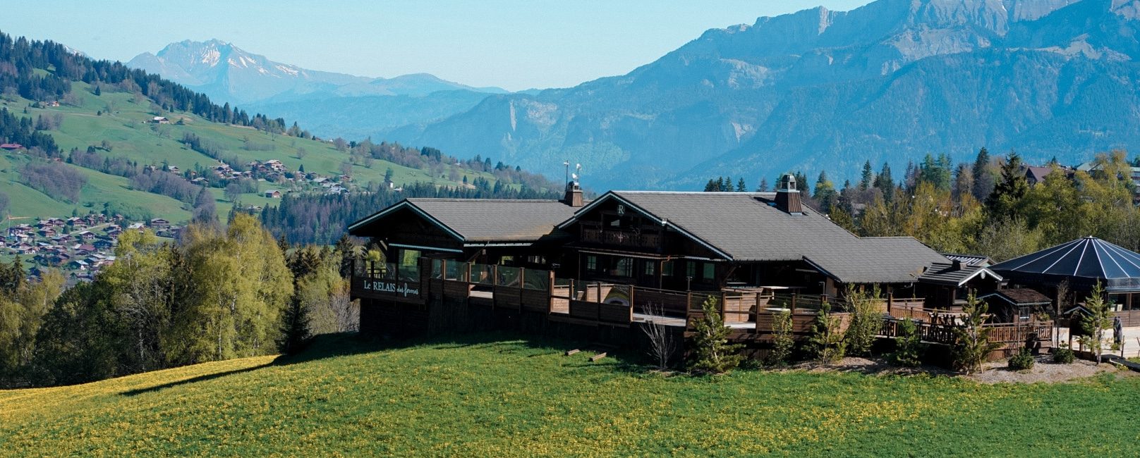 Extérieur des Fermes de Marie restaurant avec vue sur les montagnes et le restaurant.